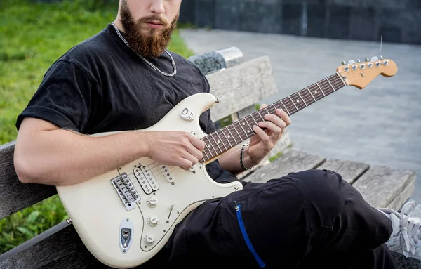 Young street musician playing guitar while sitting on the bench — 图库照片