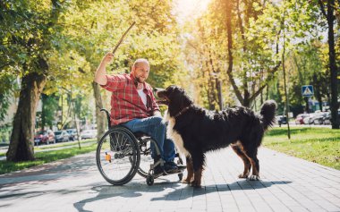 Köpeğiyle tekerlekli sandalye kullanan fiziksel engelli genç adam..