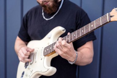 Büyük mavi duvarın yanında gitar çalan genç bir sokak müzisyeni.