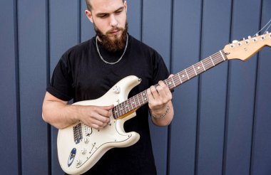 Büyük mavi duvarın yanında gitar çalan genç bir sokak müzisyeni.