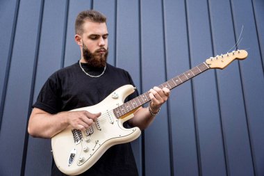 Büyük mavi duvarın yanında gitar çalan genç bir sokak müzisyeni.