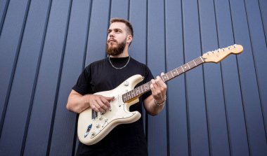 Büyük mavi duvarın yanında gitar çalan genç bir sokak müzisyeni.
