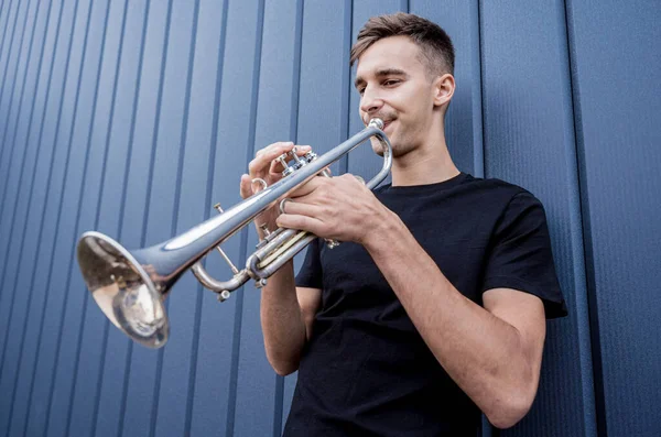 Joven músico callejero tocando la trompeta cerca de la gran pared azul — Foto de Stock