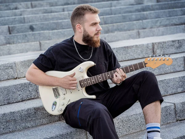 Jeune musicien de rue jouant de la guitare assis sur des marches de granit — Photo