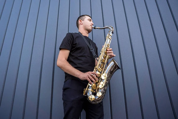 Joven músico callejero tocando el saxofón cerca de la gran pared azul — Foto de Stock