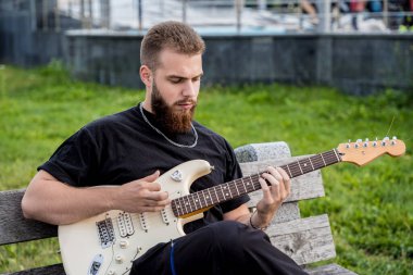 Genç sokak müzisyeni bankta otururken gitar çalıyor.