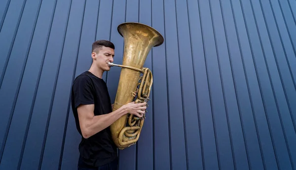 Joven músico callejero tocando la tuba cerca de la gran pared azul — Foto de Stock