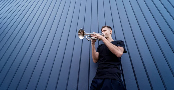 Young street musician playing the trumpet near the big blue wall — Stock Photo, Image