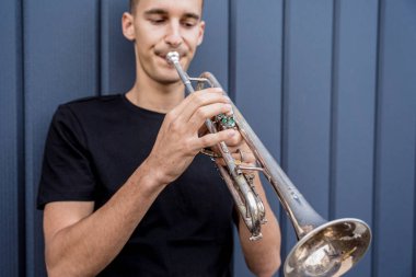 Büyük mavi duvarın yanında trompet çalan genç bir sokak müzisyeni.