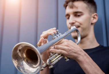 Büyük mavi duvarın yanında trompet çalan genç bir sokak müzisyeni.