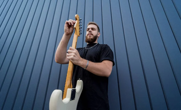 Büyük mavi duvarın yanında gitar çalan genç bir sokak müzisyeni. — Stok fotoğraf