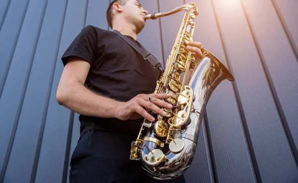 Молодой уличный музыкант играет на саксофоне у большой синей стены — стоковое фото