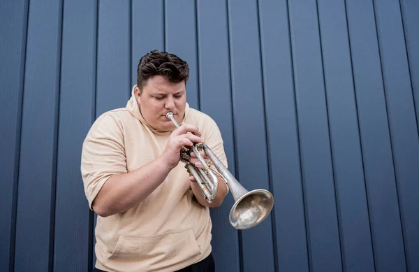 Joven músico callejero tocando la trompeta cerca de la gran pared azul — Foto de Stock