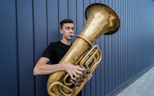 Young street musician playing the tuba near the big blue wall — Stock Photo, Image