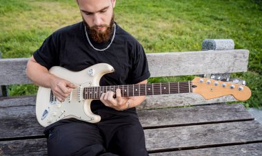 Genç sokak müzisyeni bankta otururken gitar çalıyor.