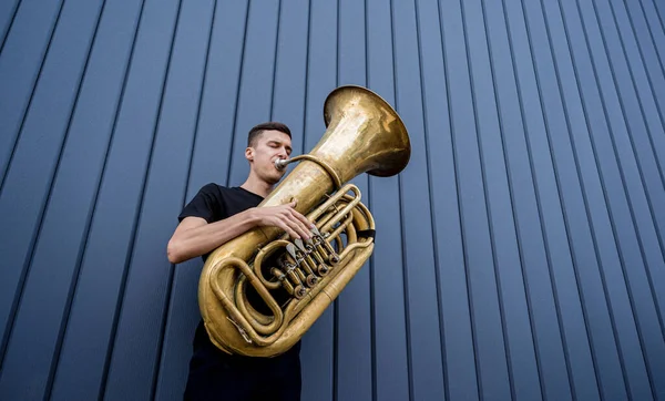 Joven músico callejero tocando la tuba cerca de la gran pared azul — Foto de Stock