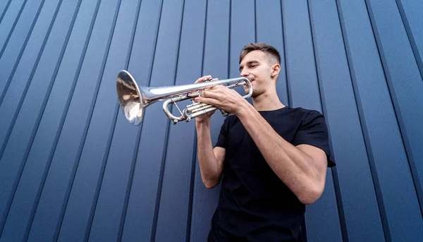 Jeune musicien de rue jouant de la trompette près du grand mur bleu — Photo