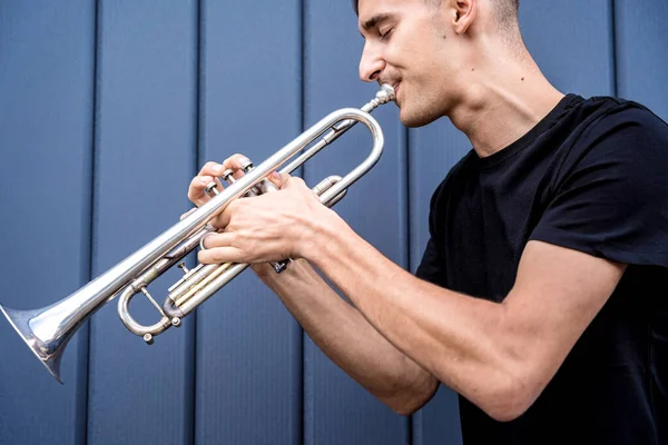 Joven músico callejero tocando la trompeta cerca de la gran pared azul — Foto de Stock