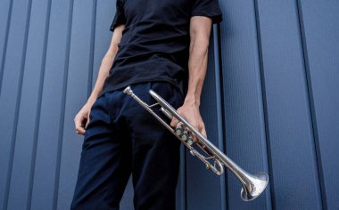 Büyük mavi duvarın yanında trompet çalan genç bir sokak müzisyeni.