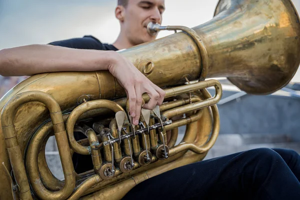 Young street musician playing tuba sitting on granite steps — Stock Photo, Image