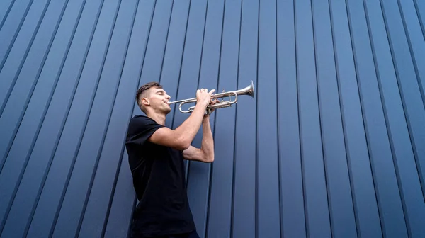 Jeune musicien de rue jouant de la trompette près du grand mur bleu — Photo