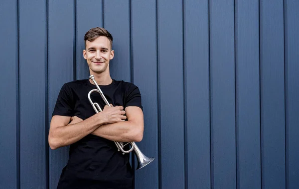 Büyük mavi duvarın yanında trompet çalan genç bir sokak müzisyeni. — Stok fotoğraf