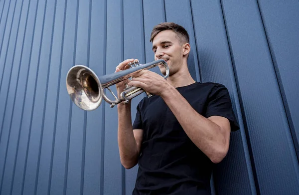 Joven músico callejero tocando la trompeta cerca de la gran pared azul — Foto de Stock