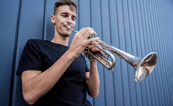 Joven músico callejero tocando la trompeta cerca de la gran pared azul — Foto de Stock