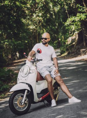 Şık bir genç adam ve motosikleti ormanda yolda.