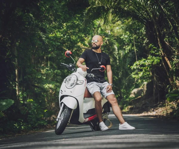 Şık bir genç adam ve motosikleti ormanda yolda.