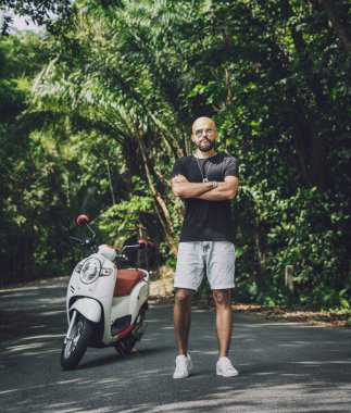 Şık bir genç adam ve motosikleti ormanda yolda.