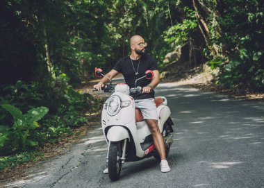 Şık bir genç adam ve motosikleti ormanda yolda.
