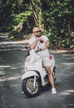 Şık bir genç adam ve motosikleti ormanda yolda.