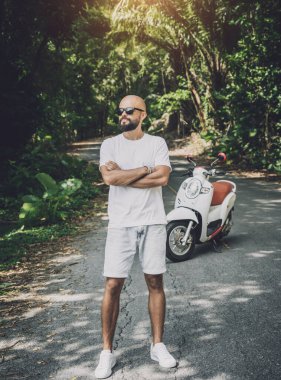 Şık bir genç adam ve motosikleti ormanda yolda.