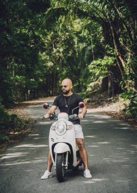 Şık bir genç adam ve motosikleti ormanda yolda.