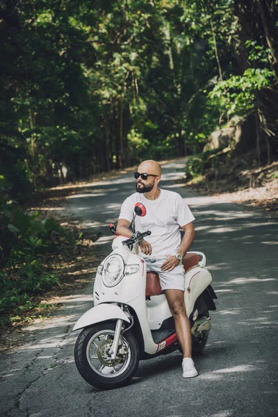 Şık bir genç adam ve motosikleti ormanda yolda.