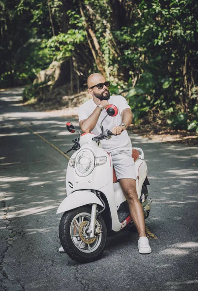 Şık bir genç adam ve motosikleti ormanda yolda.