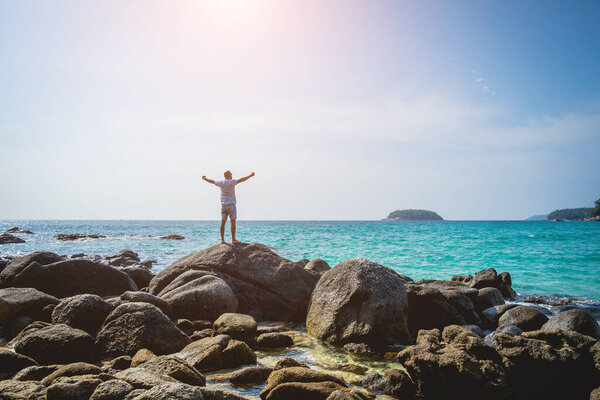 Young man relaxing on the beach while standing on an stones