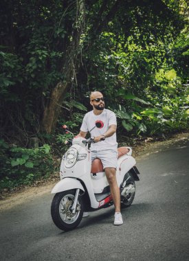 Şık bir genç adam ve motosikleti ormanda yolda.