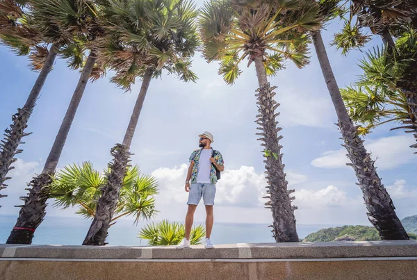 Yaz tatilinde arka planda güzel palmiyeler ve deniz manzaraları olan genç bir gezgin.