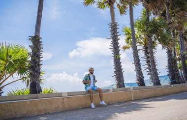 Yaz tatilinde arka planda güzel palmiyeler ve deniz manzaraları olan genç bir gezgin.