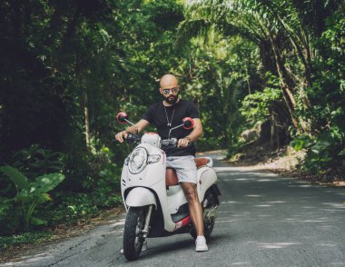Şık bir genç adam ve motosikleti ormanda yolda.