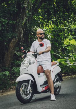 Şık bir genç adam ve motosikleti ormanda yolda.