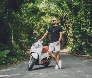 Şık bir genç adam ve motosikleti ormanda yolda.