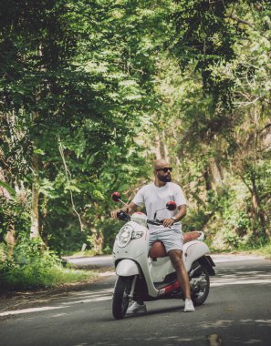 Şık bir genç adam ve motosikleti ormanda yolda.