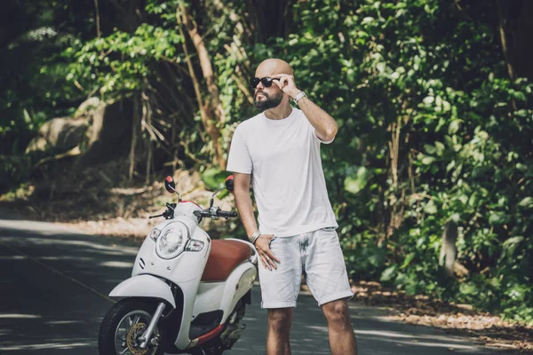 Şık bir genç adam ve motosikleti ormanda yolda.