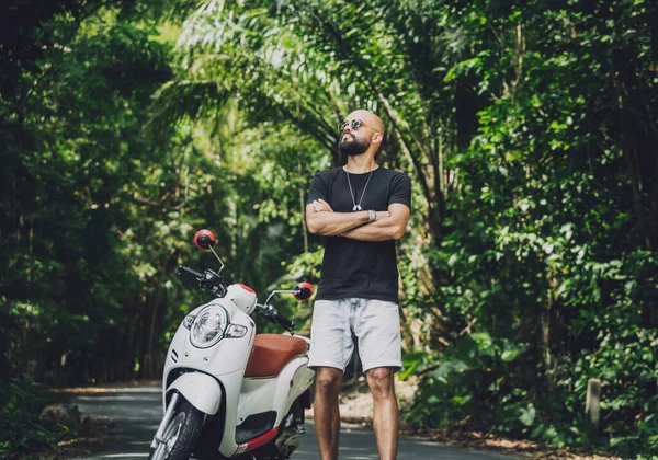 Şık bir genç adam ve motosikleti ormanda yolda.