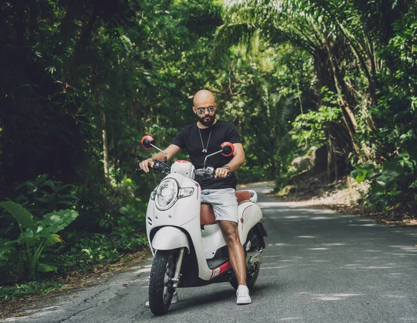 Şık bir genç adam ve motosikleti ormanda yolda.