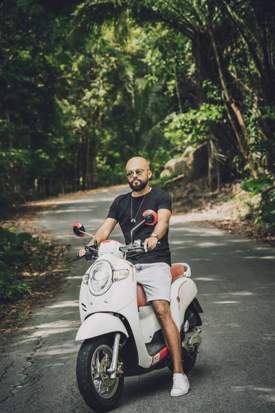 Şık bir genç adam ve motosikleti ormanda yolda.