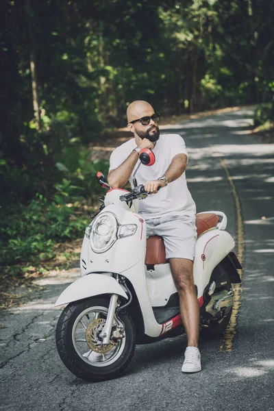 Şık bir genç adam ve motosikleti ormanda yolda.
